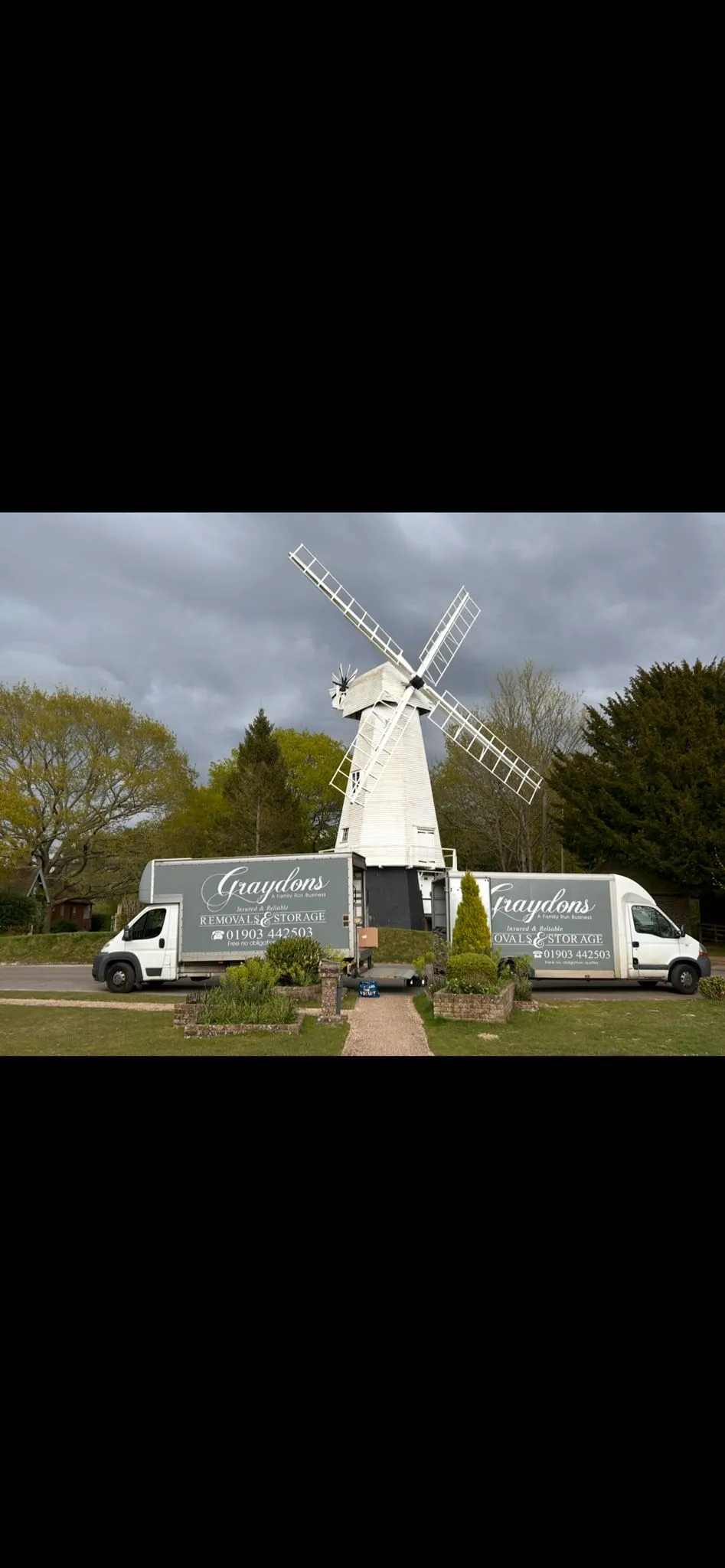 White windmill with large sails between two Graydons removal vans on a cloudy day.