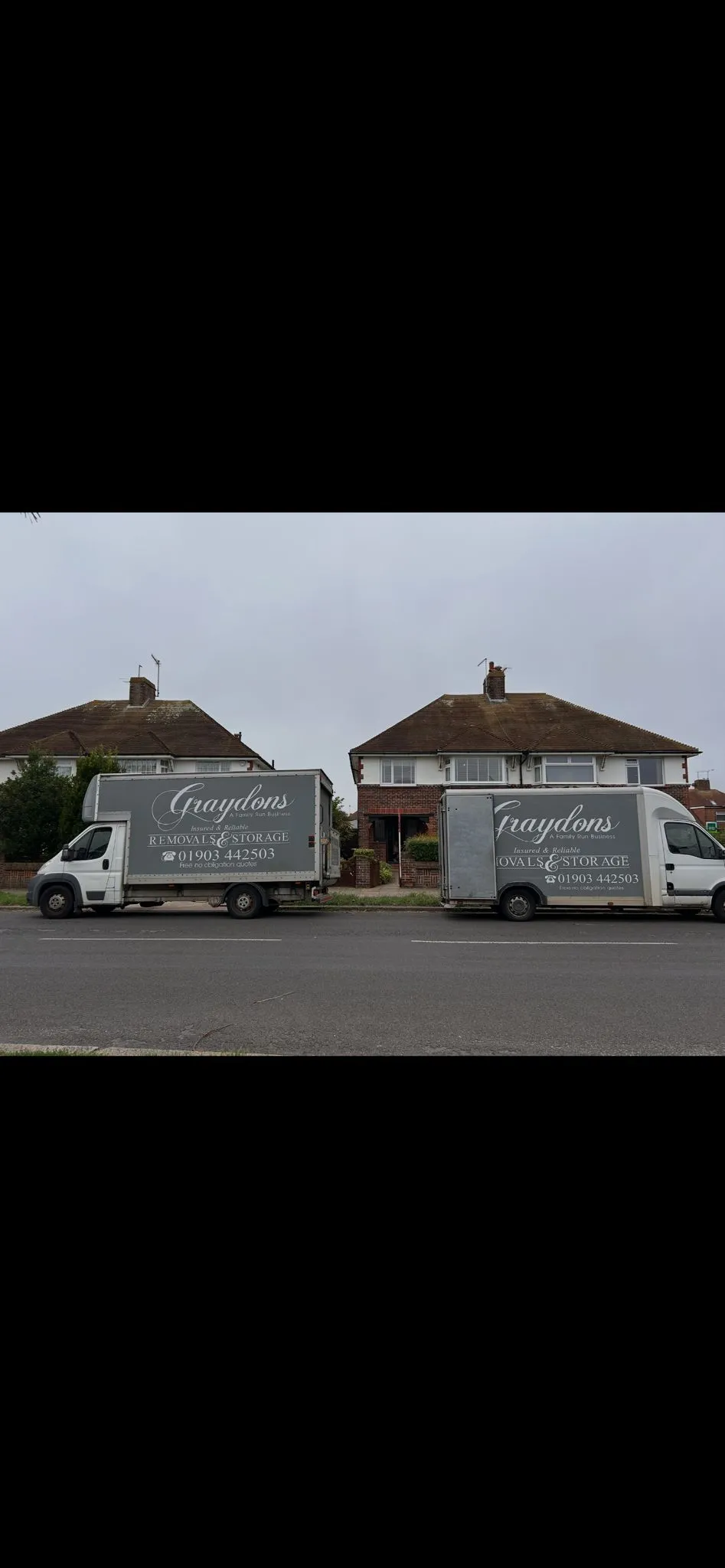 Two gray moving trucks with Graydons Removals & Storage branding parked in front of semi-detached houses.