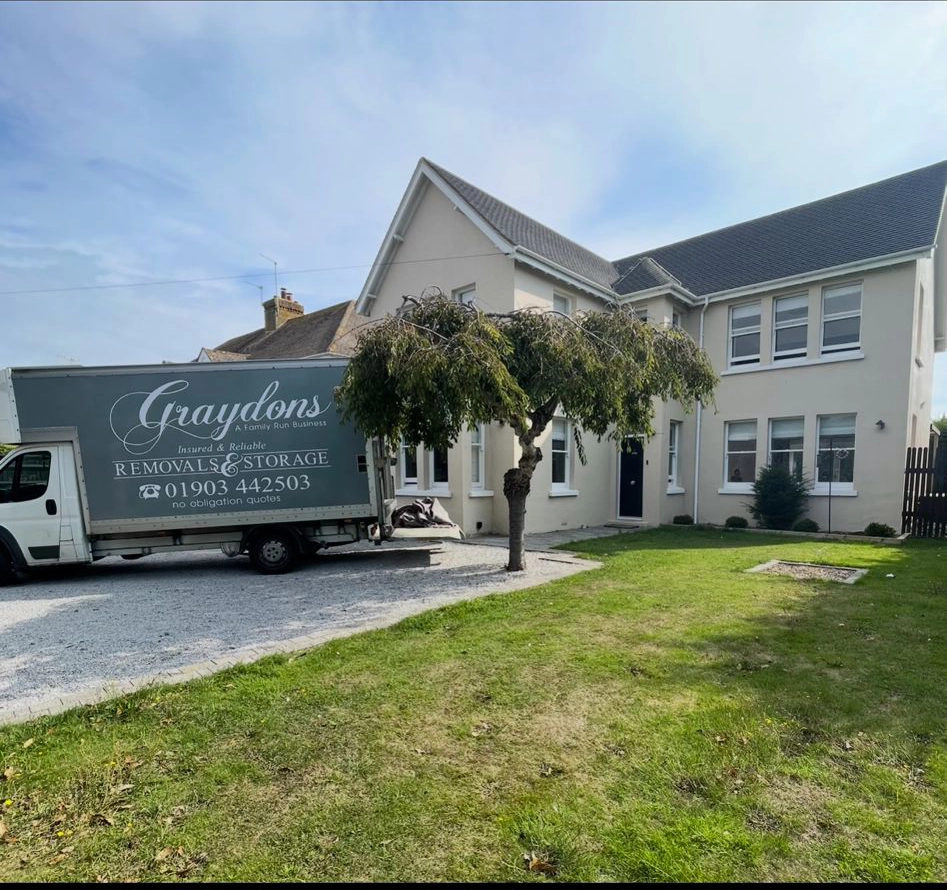 Graydons removal and storage truck parked on driveway beside a beige two-story house with a tree in front.