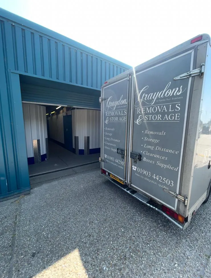 Truck with 'Graydons Removals & Storage' parked outside a unit with blue and white storage containers.