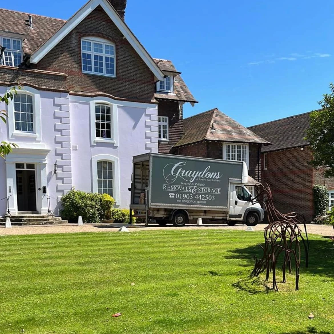 Graydons removal and storage truck parked outside a large brick and white house on a sunny day.