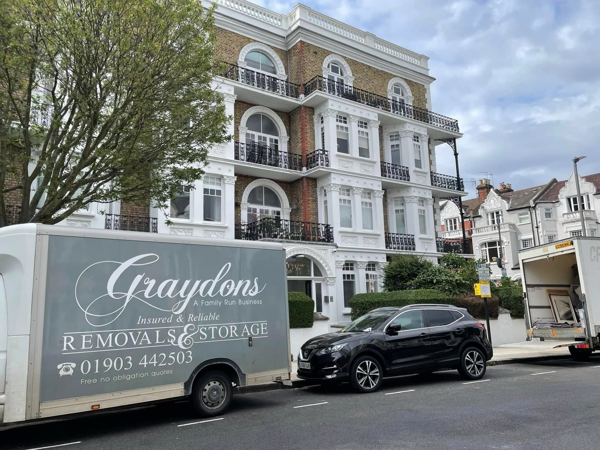 Graydons Removals & Storage truck and black SUV parked in front of a white and brick residential building.