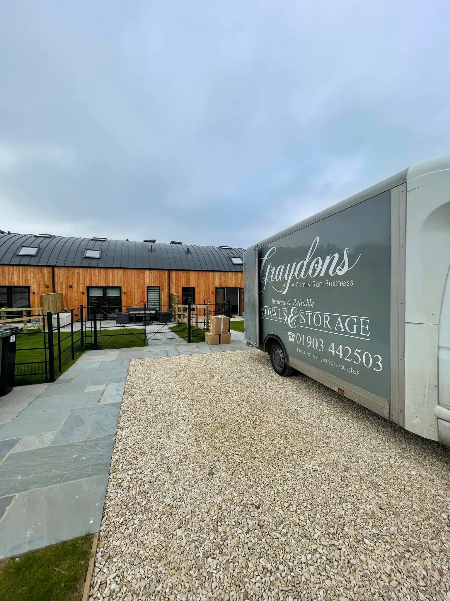 Graydons removals and storage truck parked on gravel outside modern wooden building with patio and lawn.