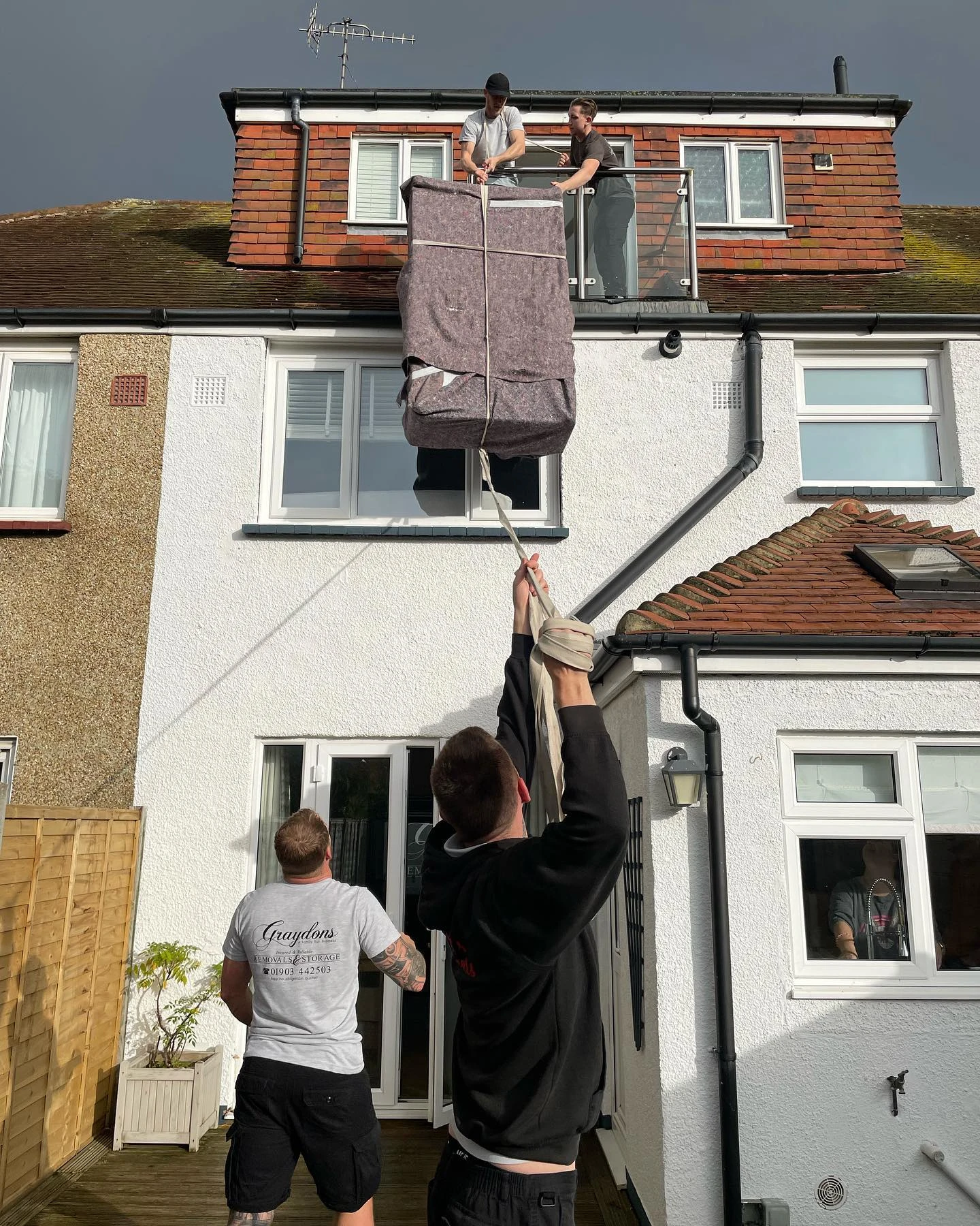three men removing a sofa from a house through a second story window